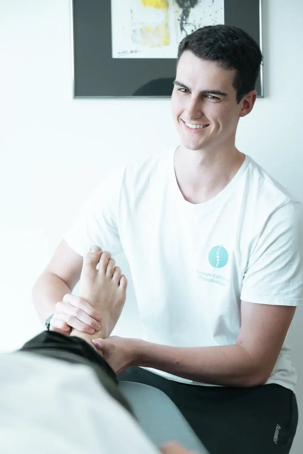 Physiotherapeut führt orthopädische Physiotherapie in Karlsruhe durch und behandelt den Fuß eines Patienten in der Praxis