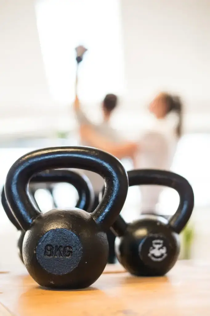 Zwei Kettlebells im Vordergrund, unscharf im Hintergrund eine Übungseinheit für klassische Krankengymnastik in der Praxis