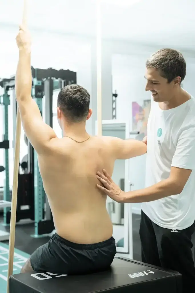 Physiotherapeut unterstützt Patienten bei klassischer Krankengymnastik mit Schulter- und Rückenübung in der Praxis